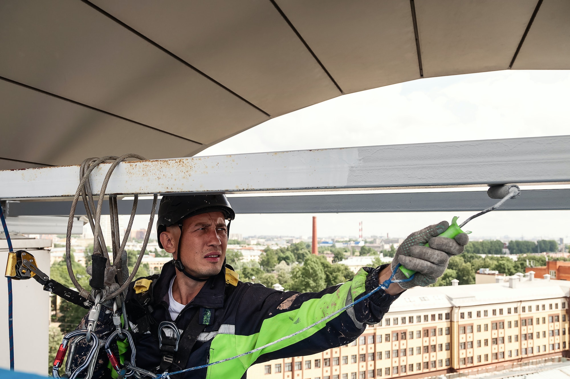 Industrial mountaineering worker in uniform hangs over building and paint roller